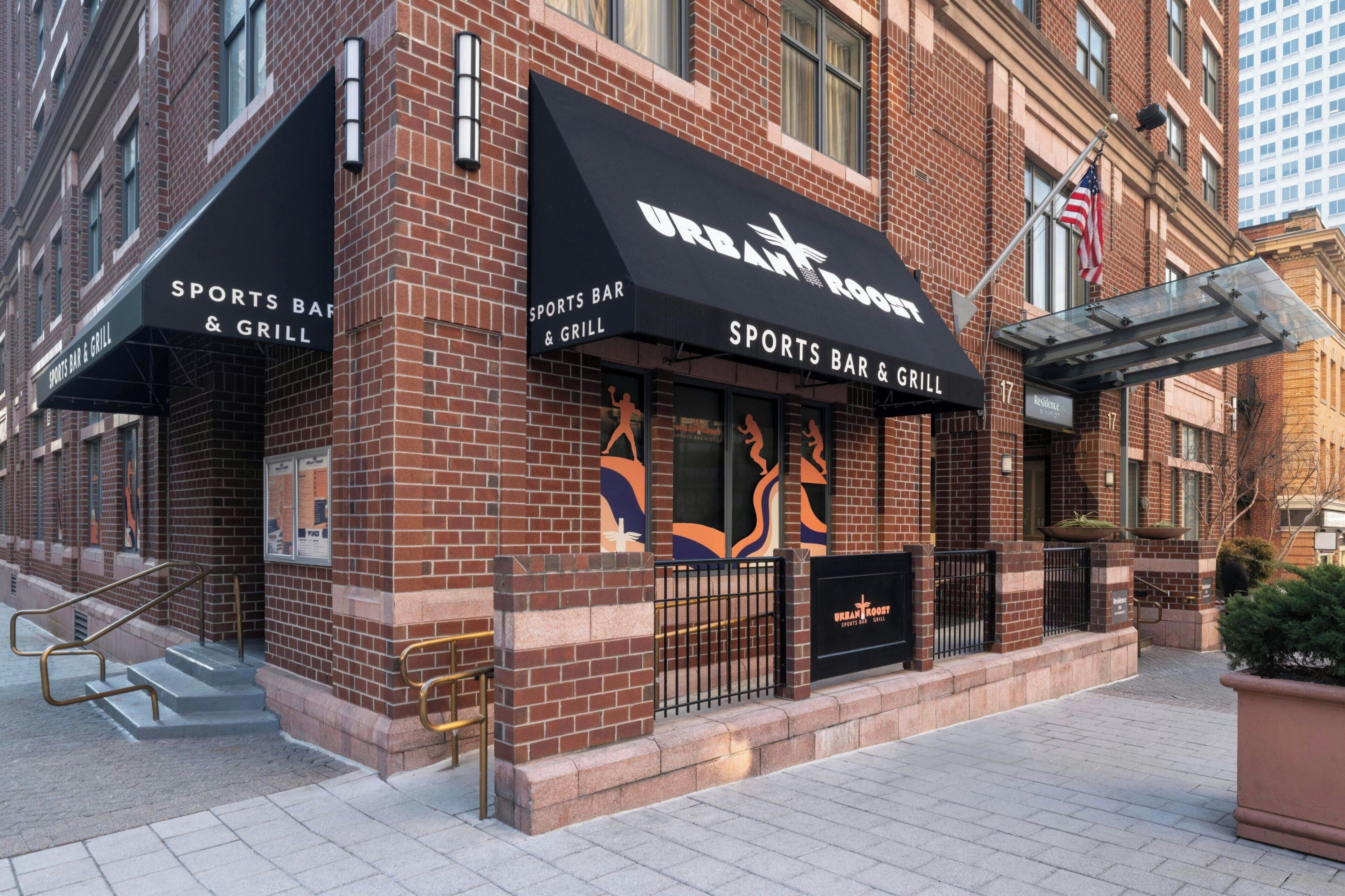 A brick building with a sports bar and grill sign, a glass entrance, and a flag.