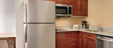 A modern kitchen with stainless steel appliances, wooden cabinets, granite countertops, and a built-in microwave.