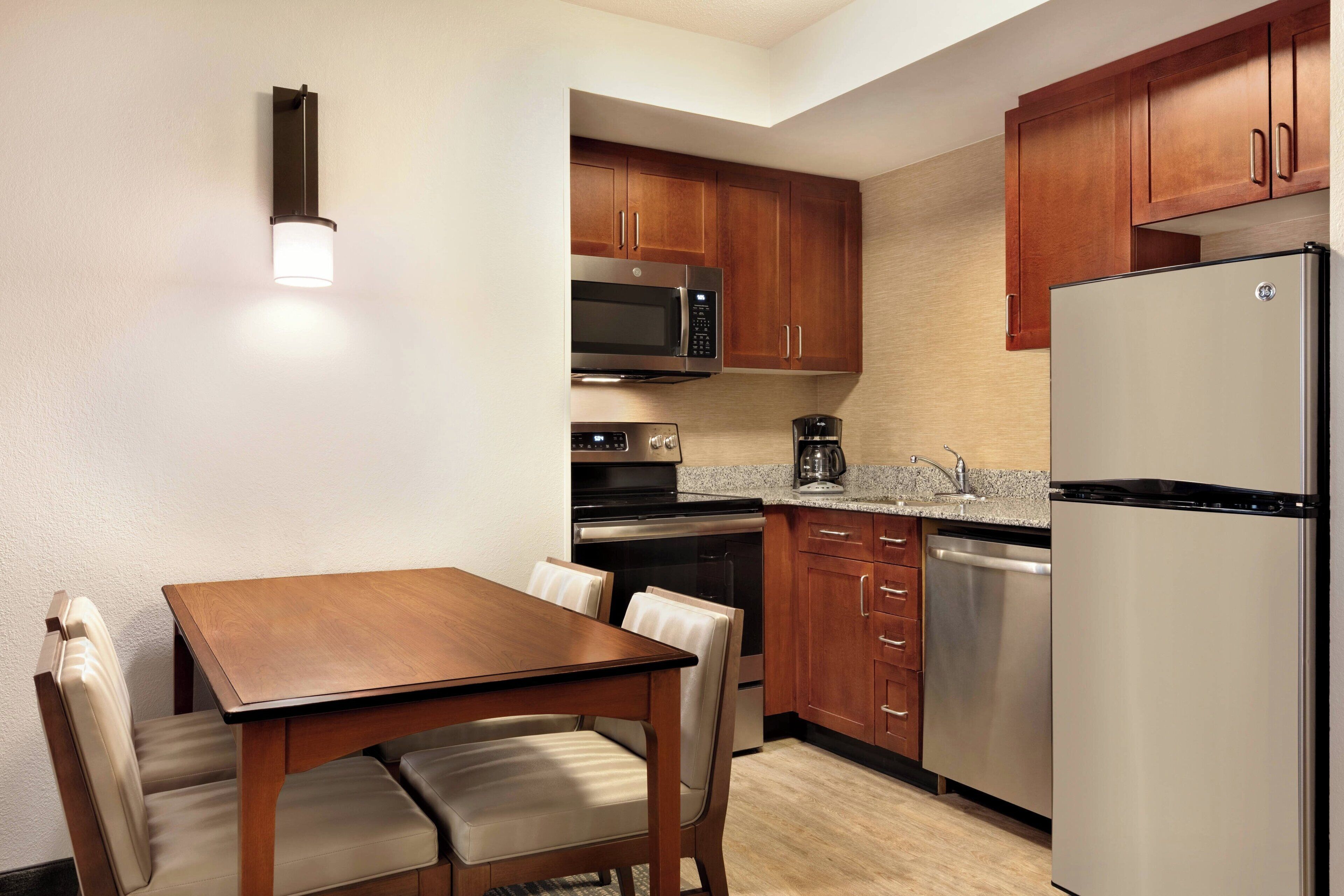 A compact kitchen with wooden cabinets, stainless steel appliances, and a dining area with a table and chairs.