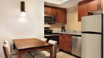 A compact kitchen with wooden cabinets, stainless steel appliances, and a dining area with a table and chairs.