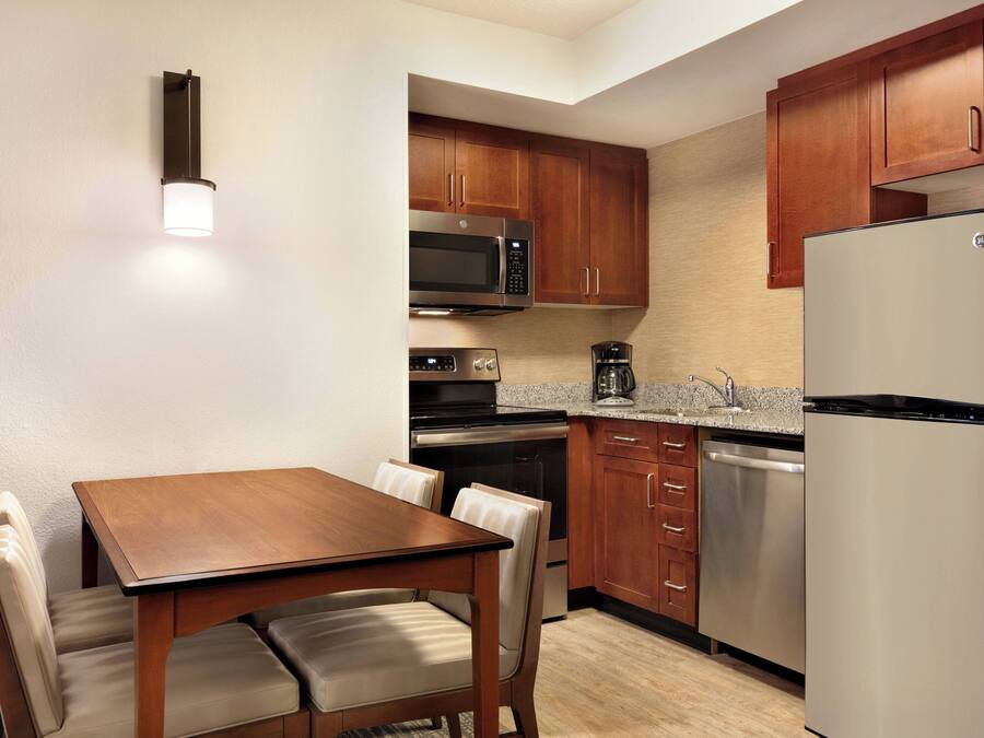 A compact kitchen with wooden cabinets, stainless steel appliances, and a dining area with a table and chairs.