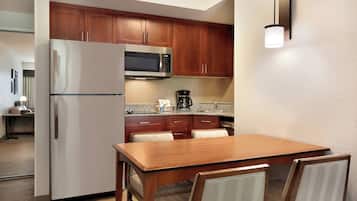 A compact kitchen with wooden cabinets, a stainless steel refrigerator, a microwave, and a coffee maker.