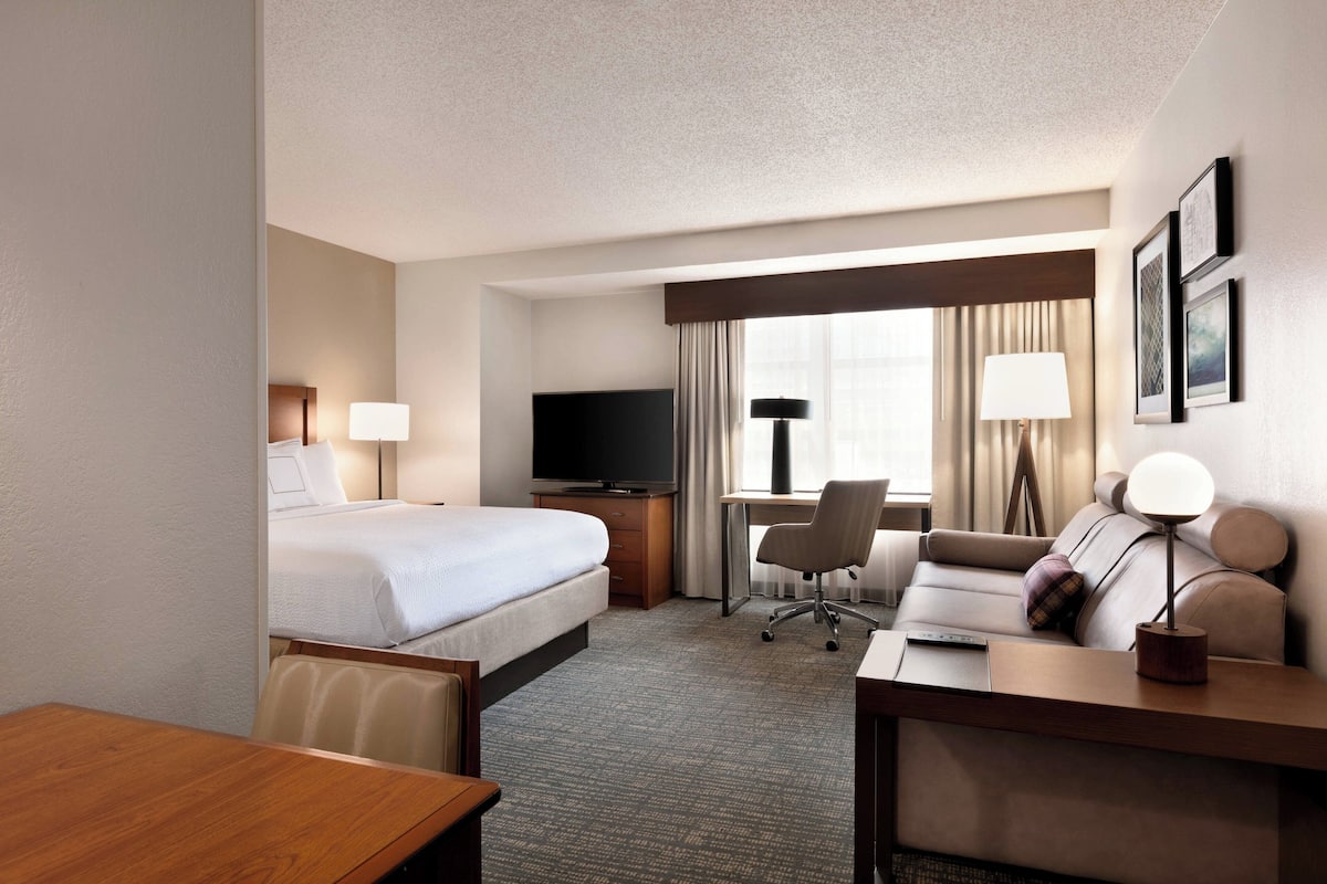 A hotel room with a bed, desk, chair, TV, and lamp.