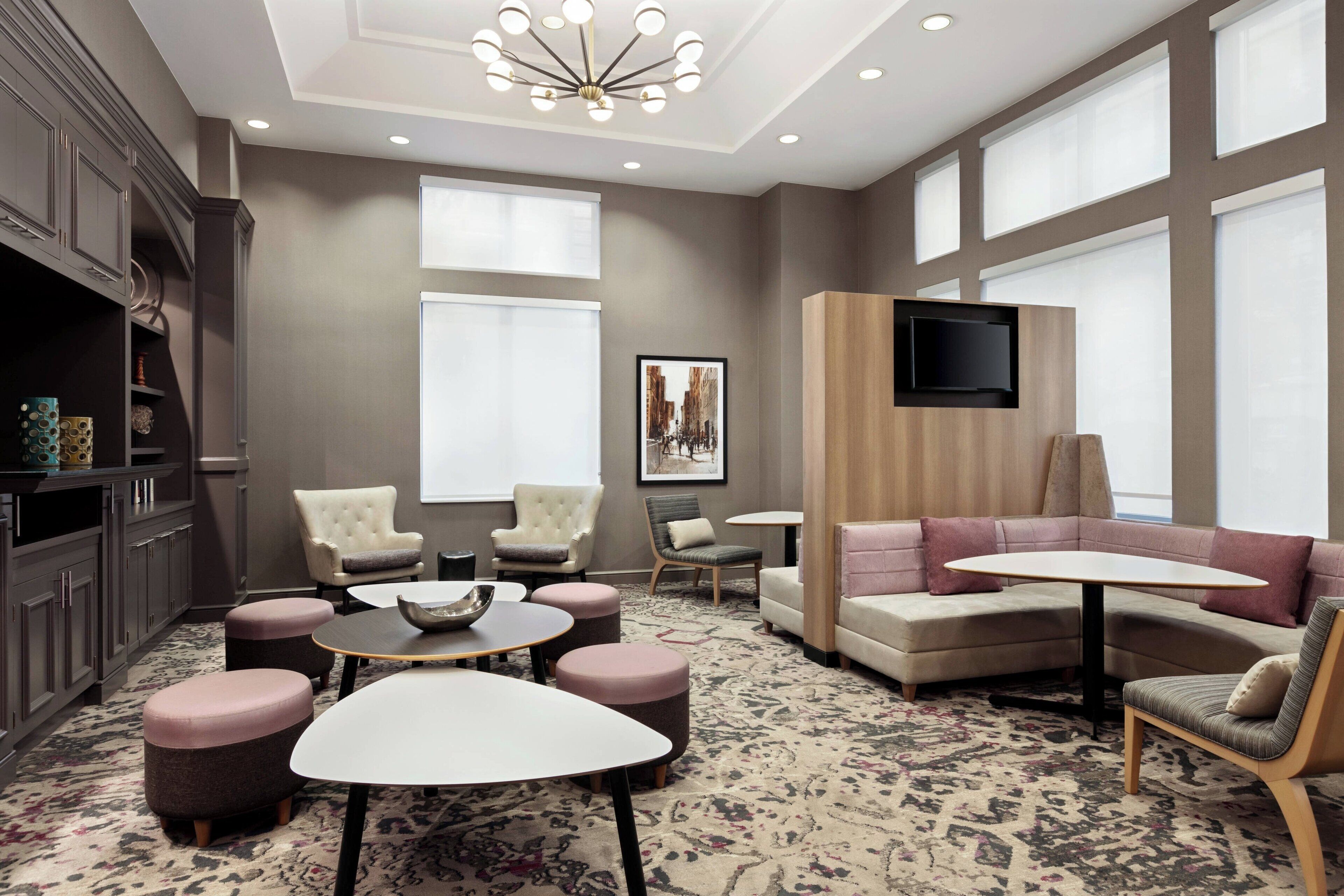 A modern lounge area with a sofa, chairs, ottomans, a table, and a TV mounted on the wall.