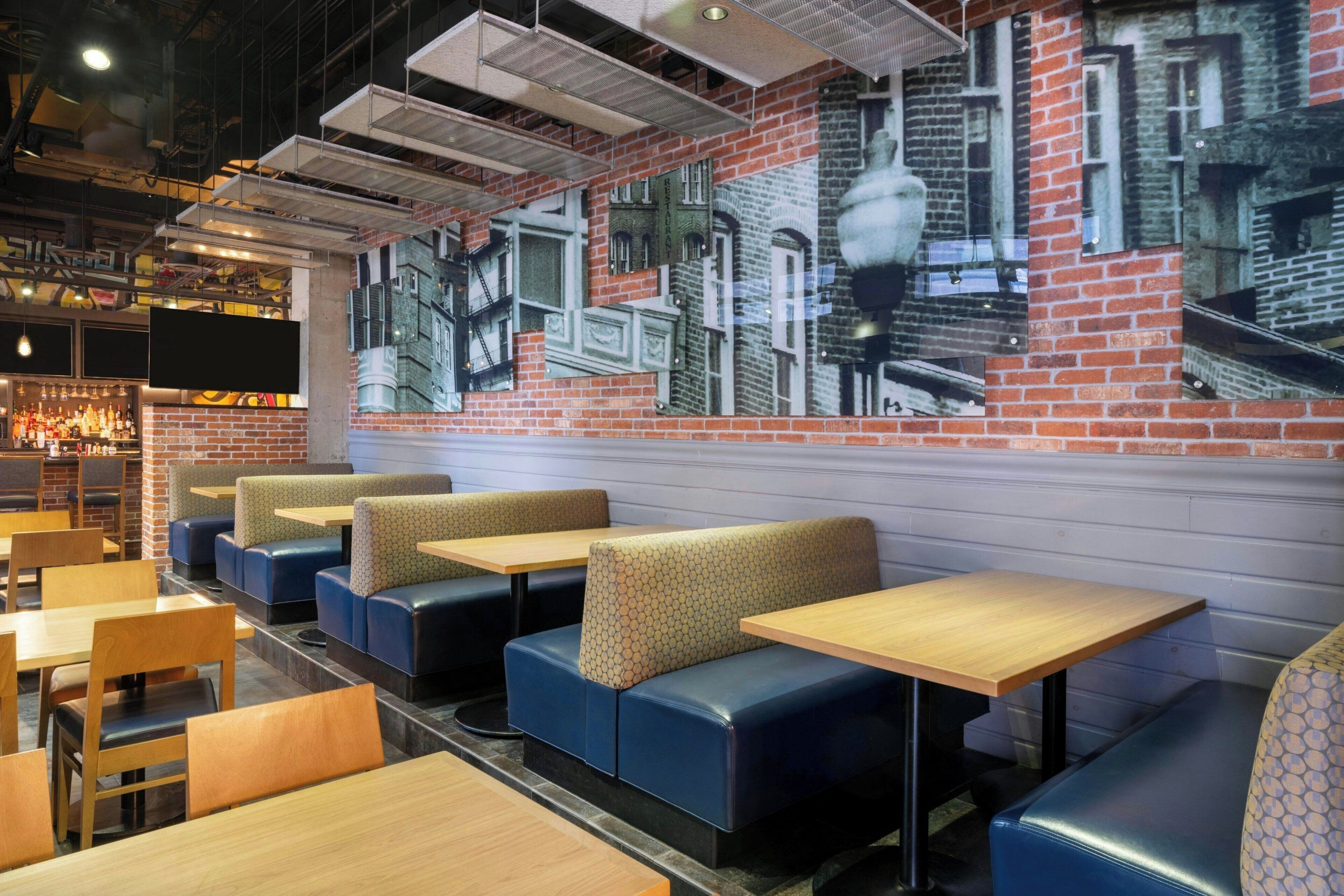 Interior de restaurante com cabines, mesas e um mural de parede de tijolos.