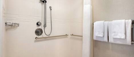 A shower with a handheld showerhead and a handheld hose, a towel rack with towels, and a handrail.