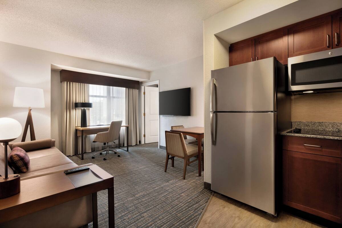 A hotel room with a bed, a desk with a chair, a refrigerator, a microwave, and a flat-screen TV.