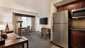 A hotel room with a bed, a desk with a chair, a refrigerator, a microwave, and a flat-screen TV.