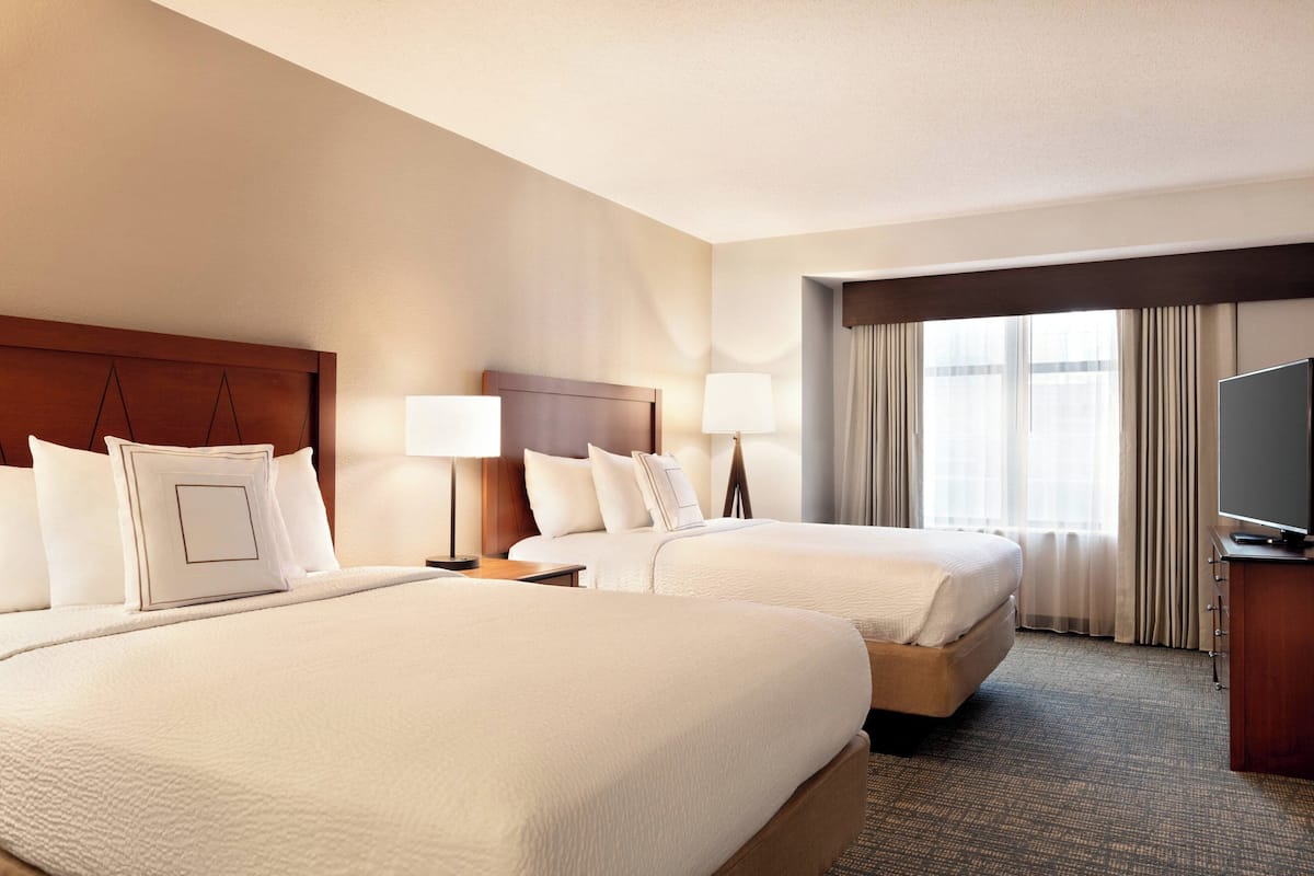 A hotel room with two beds, a television, and a window with curtains.