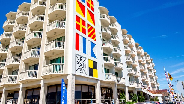 A multi-story hotel with balconies, a prominent logo, and a clear blue sky. - Port Royal Oceanfront Hotel (Wildwood Crest)