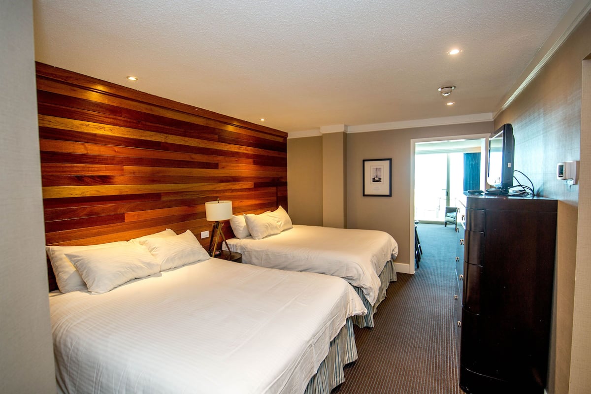 Habitación de hotel con dos camas, cabecera de madera, cómoda y un cuadro en la pared.
