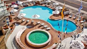 A pool area with multiple swimming pools, lounge chairs, umbrellas, and flags. - Port Royal Oceanfront Hotel (Wildwood Crest)