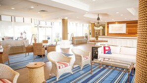 A spacious lobby with wicker furniture, a striped carpet, and a white sofa with a red pillow. - Port Royal Oceanfront Hotel (Wildwood Crest)