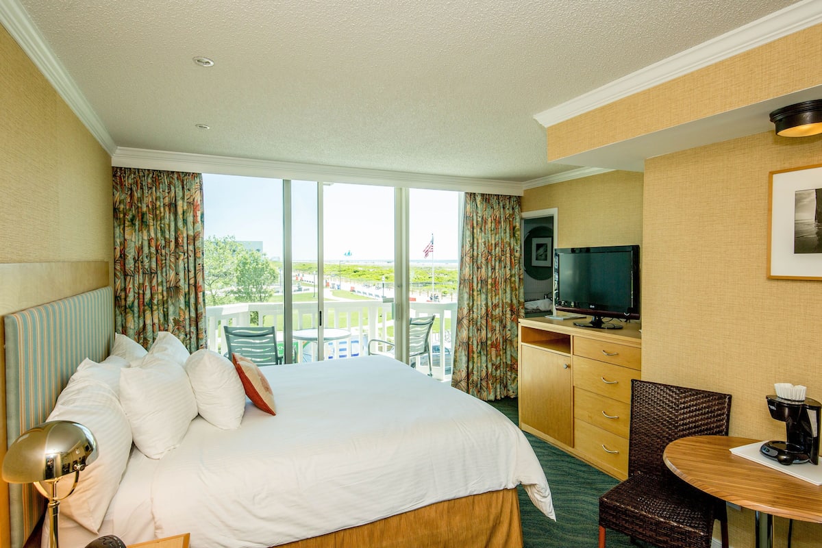 Habitación de hotel con una cama grande, televisión, mesa de comedor con sillas y vistas al exterior.