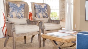Two wooden armchairs with blue patterned cushions, a wooden coffee table, and a view of a building through a window. - Port Royal Oceanfront Hotel (Wildwood Crest)