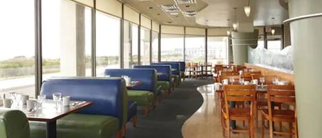 Un restaurante con asientos en tono azul y verde, mesas de madera y vista a la ciudad.