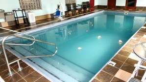 En inomhuspool med ett kaklat golv, en poolstege och några solstolar.