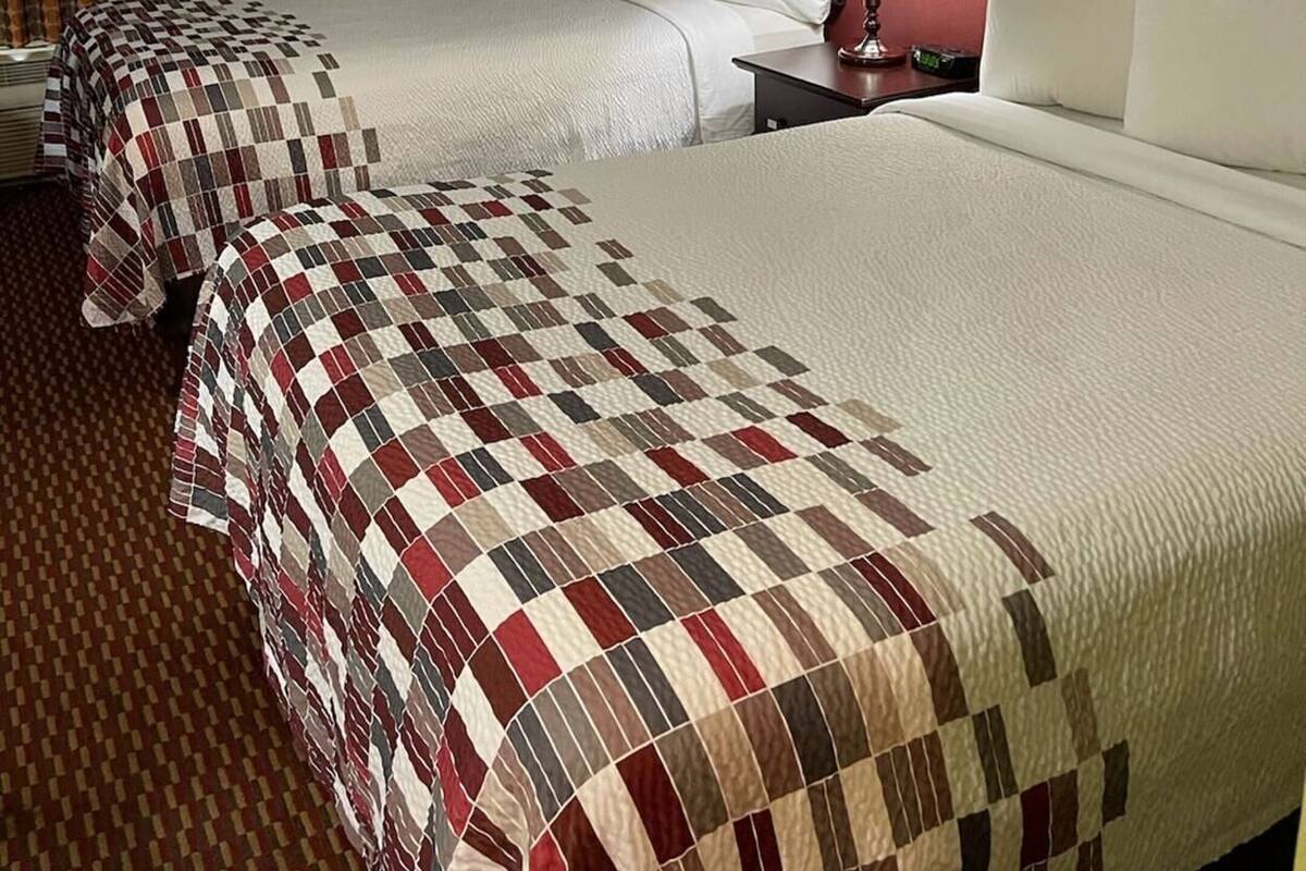 Ein Hotelzimmer mit zwei Betten, einem Nachttisch mit Lampe, einem Fenster mit Vorhängen und einem gerahmten Bild an der Wand.