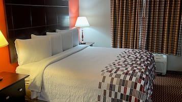 Une chambre d’hôtel avec un grand lit, une table de chevet, une lampe, un téléviseur fixé au mur et une fenêtre avec des rideaux.