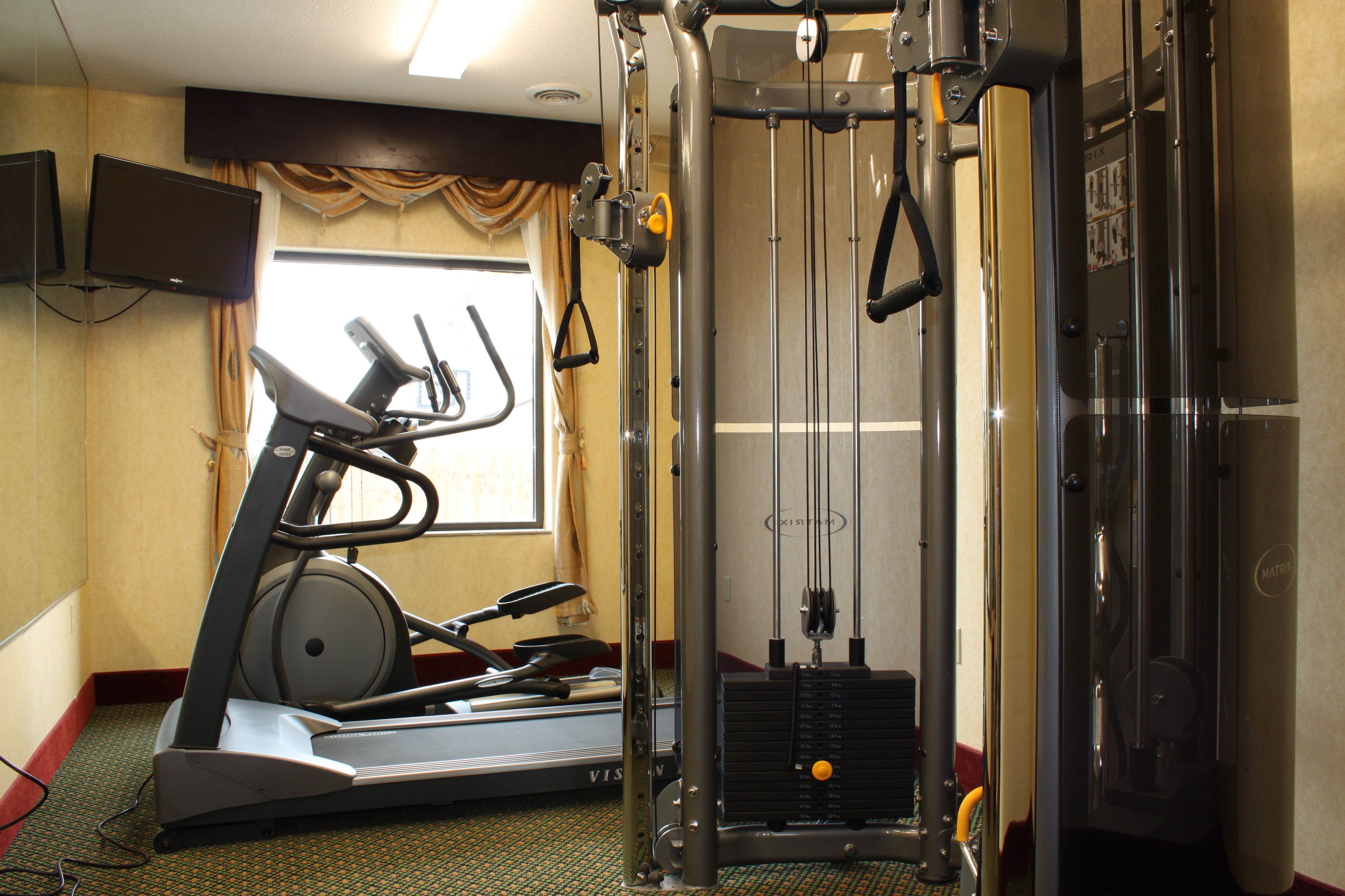 A gym with exercise equipment including a treadmill, weight machines, and a cable machine.