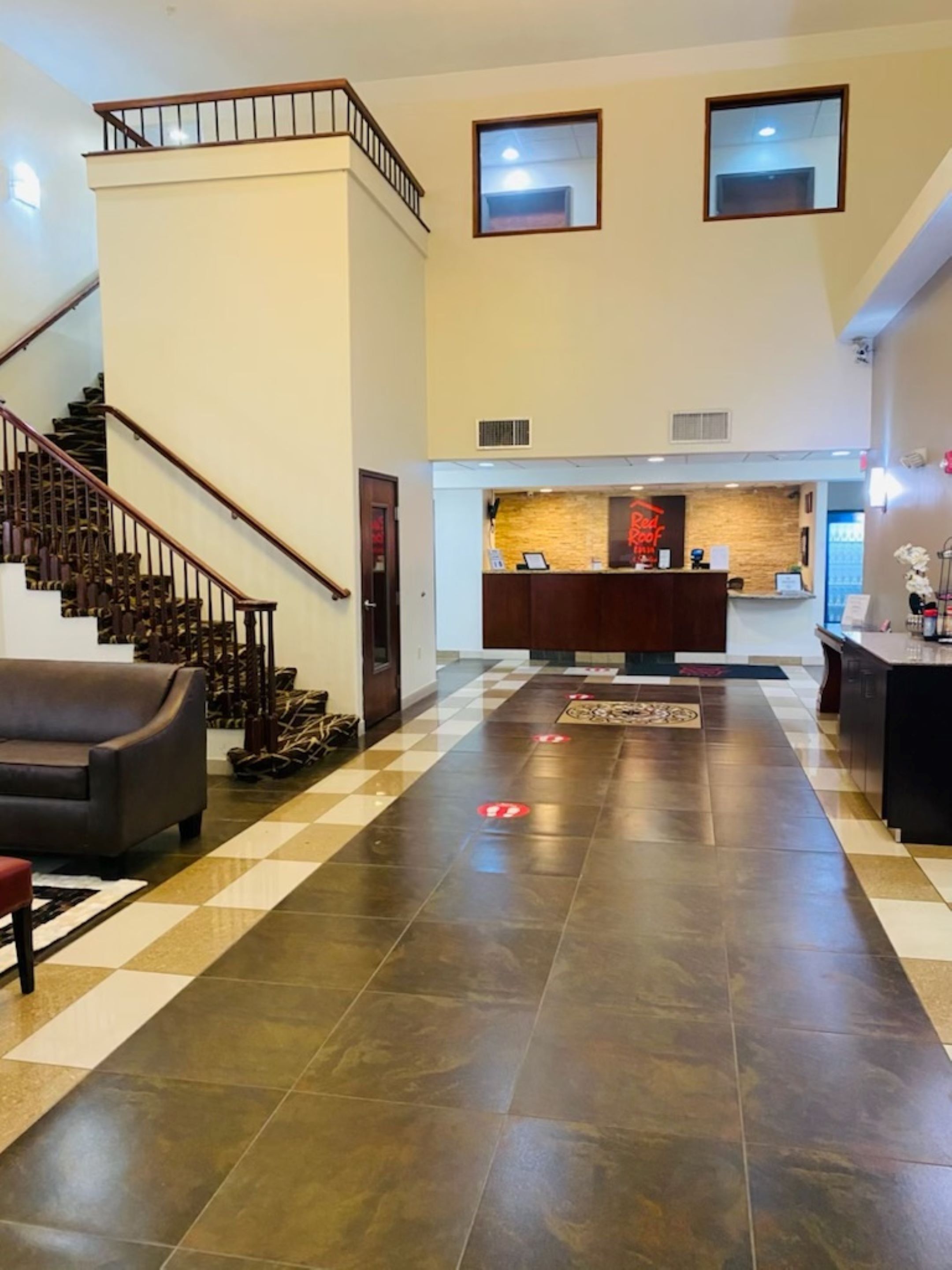 Un'hall d'albergo con pavimento a scacchi, una reception, una scalinata e un divano.