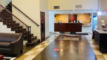 Un'hall d'albergo con pavimento a scacchi, una reception, una scalinata e un divano.
