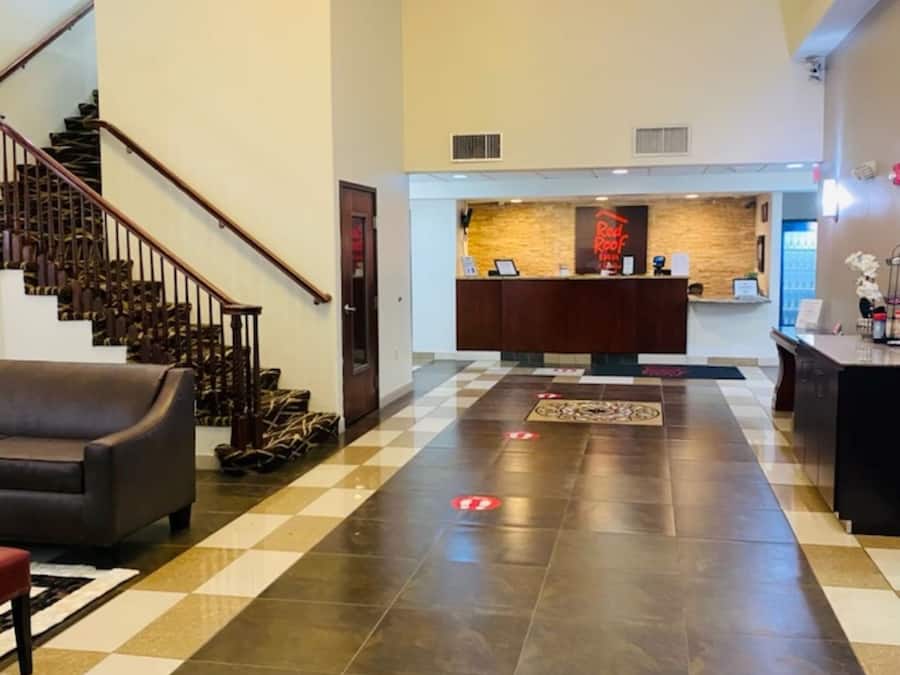 A hotel lobby with a checkered floor, a reception desk, a staircase, and a sofa.