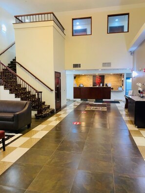 A hotel lobby with a checkered floor, a reception desk, a staircase, and a sofa. - Red Roof Inn & Suites Detroit-Melvindale/ Dearborn (Melvindale)