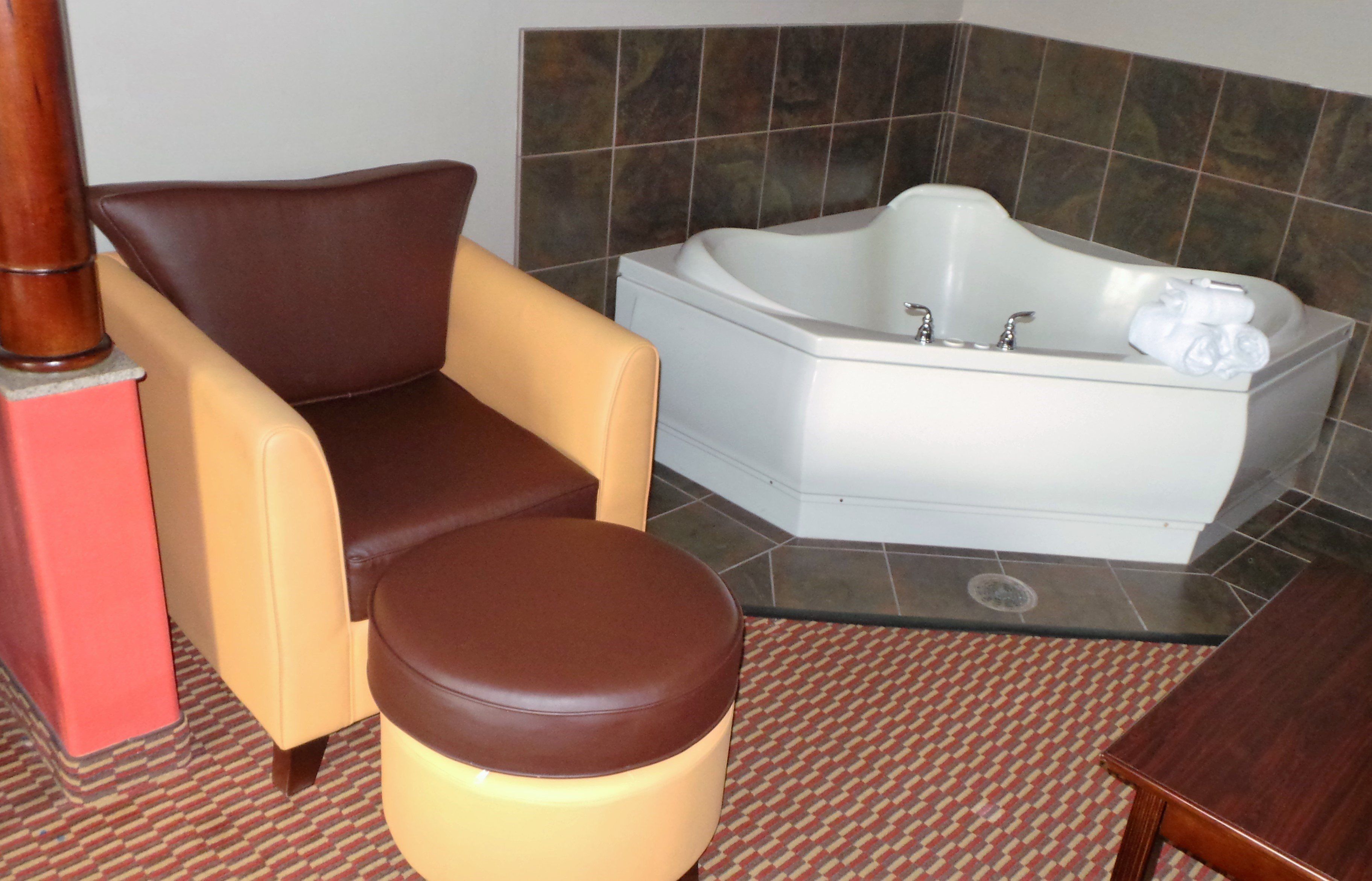A bathroom with a bathtub, a chair, and a small stool.