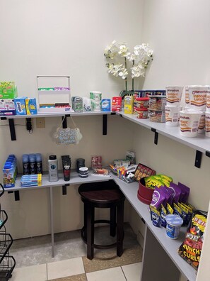 A kitchenette with shelves stocked with food items, a coffee machine, and a small stool. - Red Roof Inn & Suites Detroit-Melvindale/ Dearborn (Melvindale)