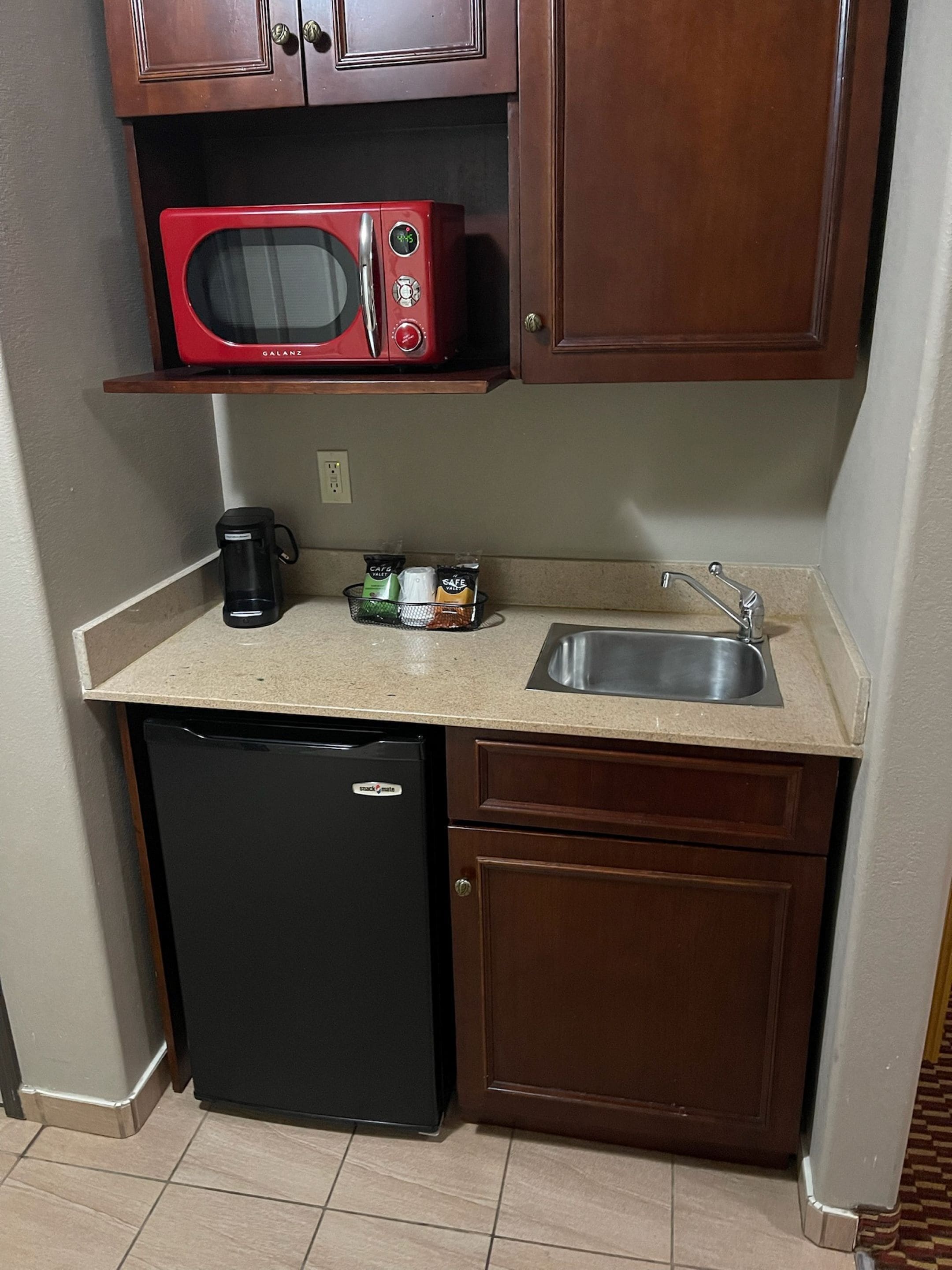 Una cocina compacta con microondas, cafetera y lavamanos.