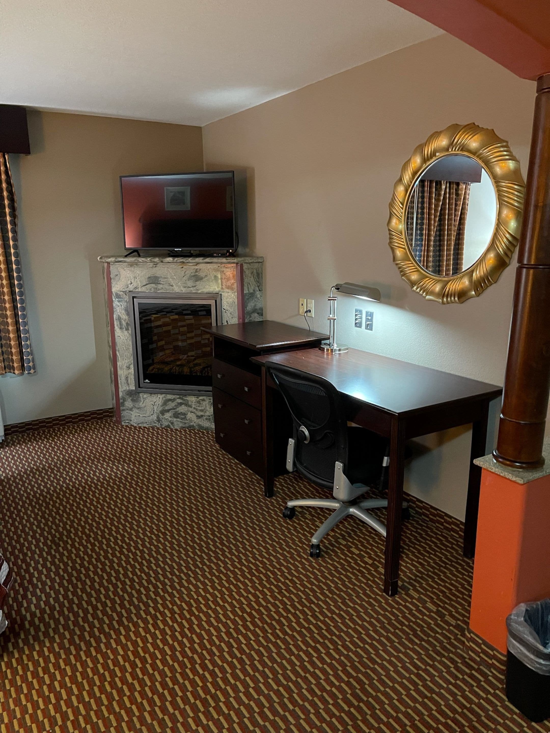 Une chambre d’hôtel équipée d’une cheminée, d’un bureau, d’une chaise, d’une télévision et d’un miroir.