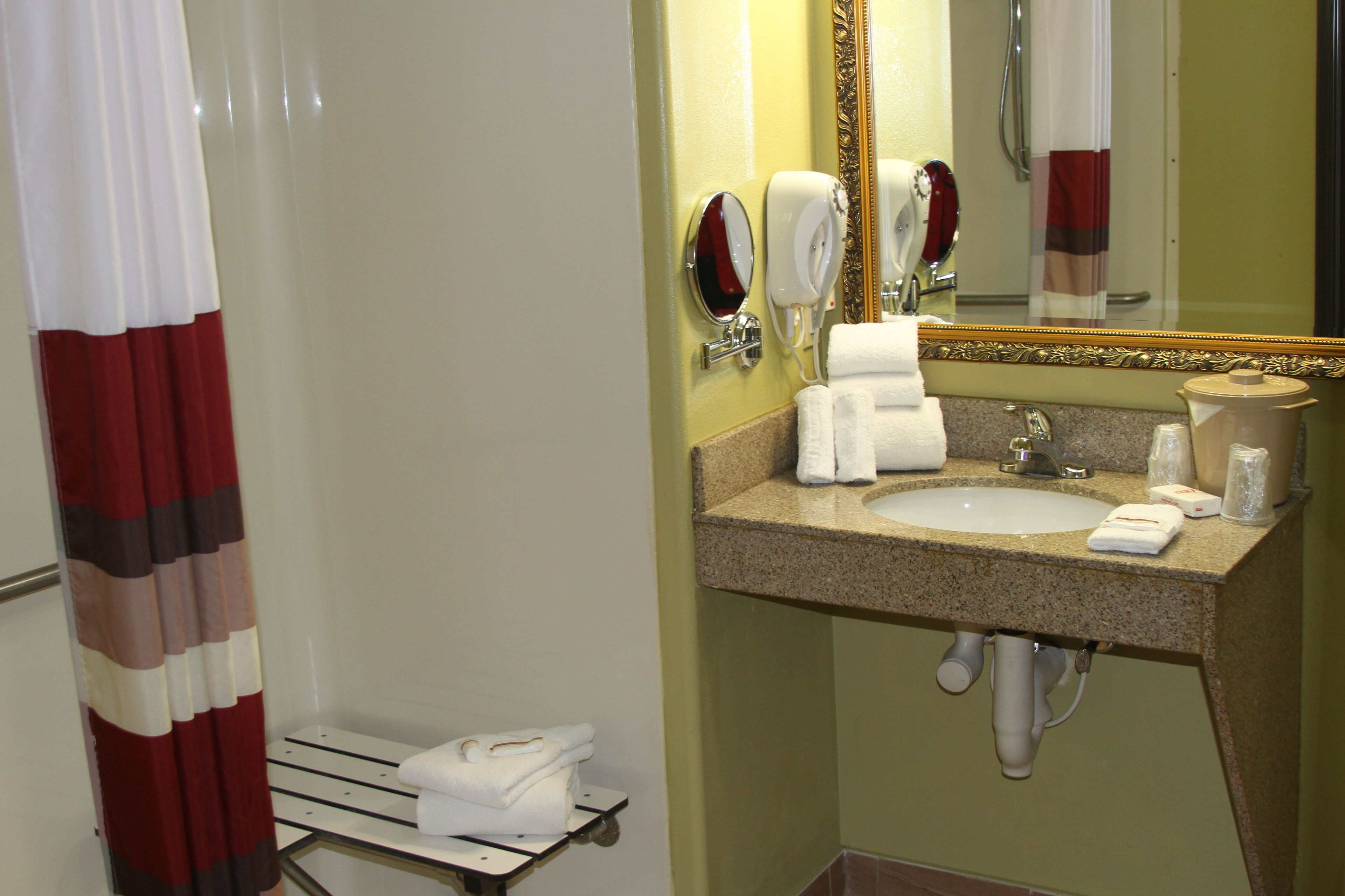 A hotel bathroom with a sink, mirror, towel rack, and shower curtain.