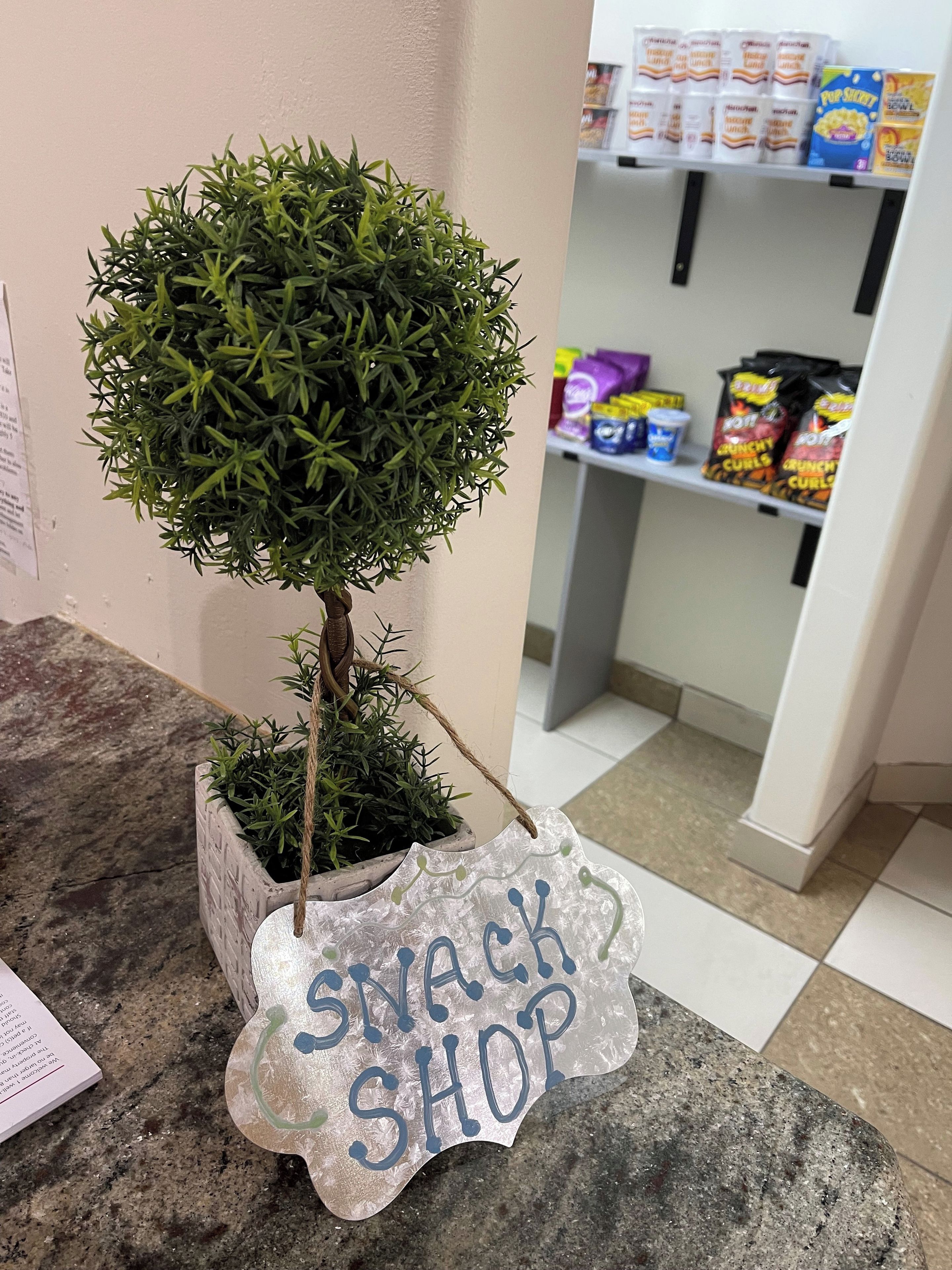 A potted tree with a sign that reads 'SNACK SHOP' in a commercial setting.