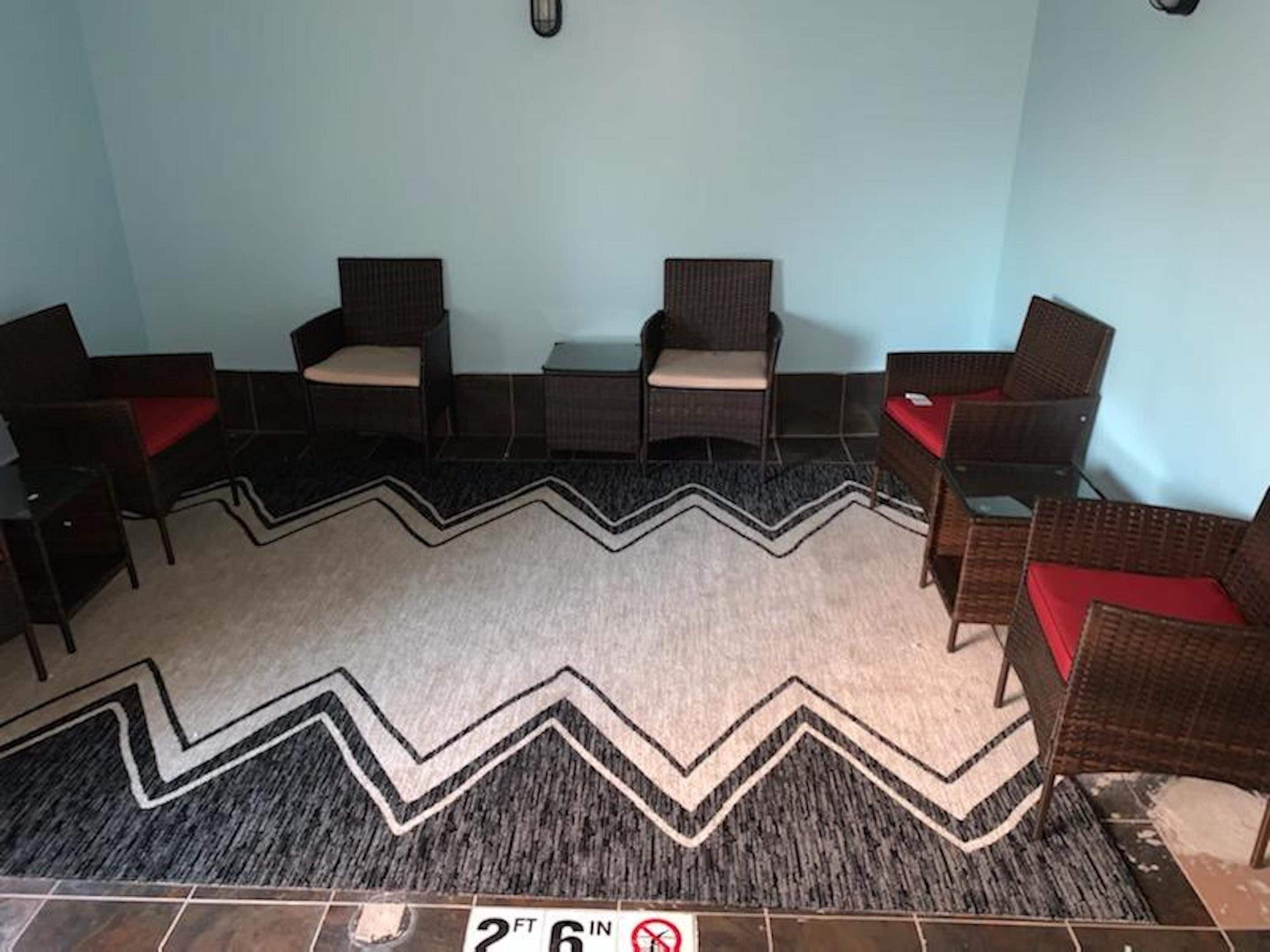 A room with a zigzag patterned rug, four wicker chairs with red cushions, and a tiled floor.