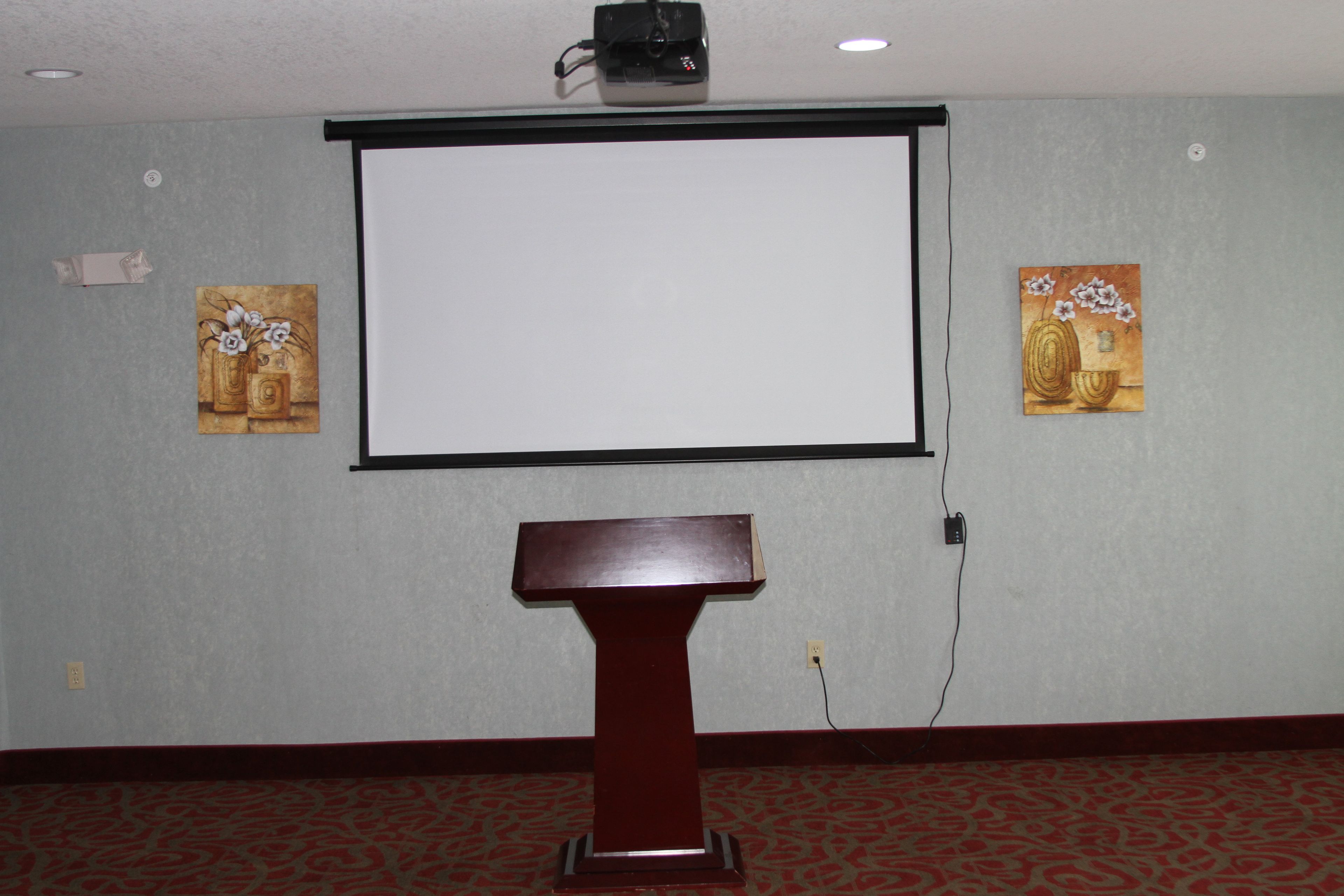 A conference room with a projector screen, a podium, and two paintings on the walls.