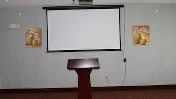 A conference room with a projector screen, a podium, and two paintings on the walls.