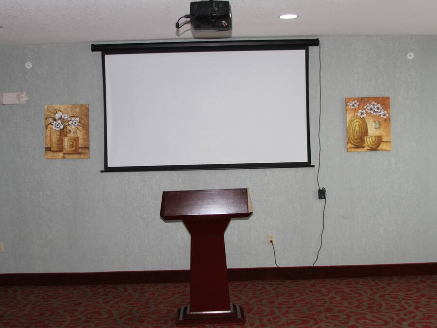 Un salón de conferencias con una pantalla de proyector, un atril y dos cuadros en las paredes.