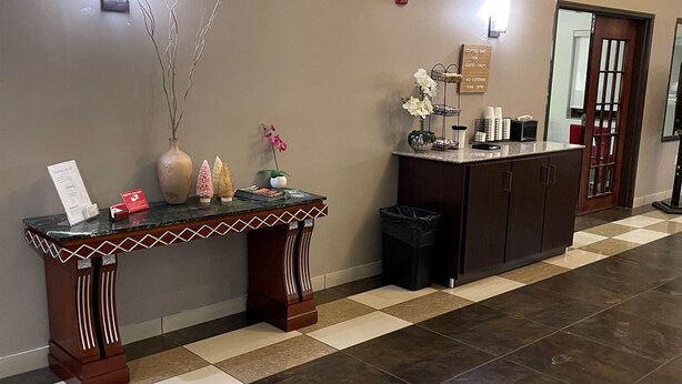 A reception area with a checkered floor, a decorative vase, a small table with a sign, and a coffee station. - Red Roof Inn & Suites Detroit-Melvindale/ Dearborn (Melvindale)