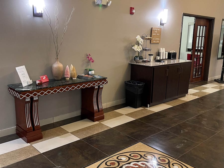 Una zona de recepción con suelo a cuadros, un jarrón decorativo, una mesa pequeña con un letrero y una estación de café.