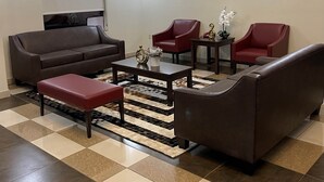 A spacious living area with a brown leather sofa, two red armchairs, a coffee table, and a patterned rug. - Red Roof Inn & Suites Detroit-Melvindale/ Dearborn (Melvindale)