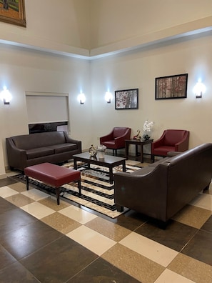 A spacious living area with a brown leather sofa, two red armchairs, a coffee table, and a patterned rug. - Red Roof Inn & Suites Detroit-Melvindale/ Dearborn (Melvindale)