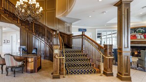 A grand staircase with a chandelier, a reception desk, and a fireplace. - Madison Beach Hotel (Madison)