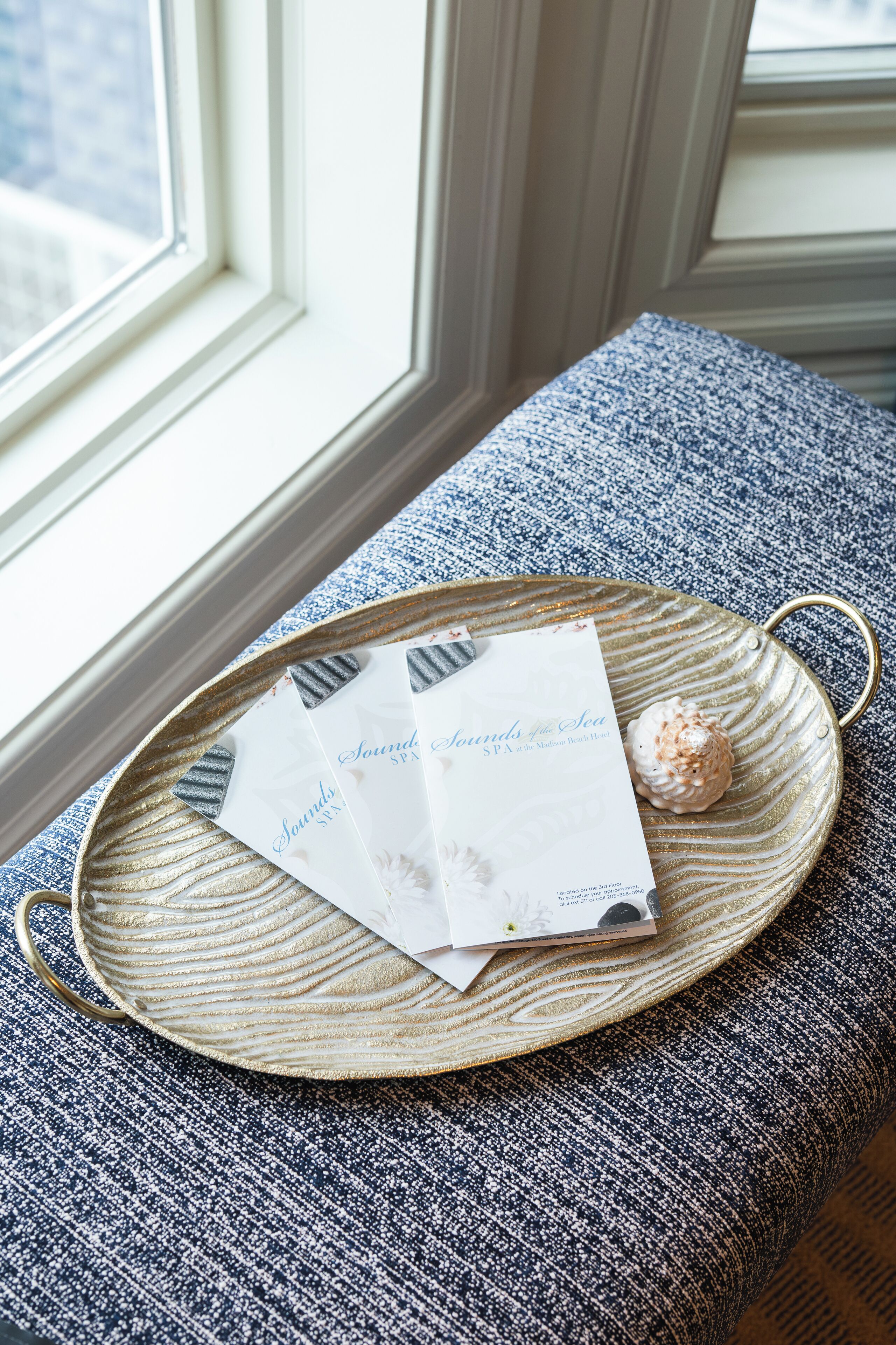 A tray with a menu and a dessert on a textured blue and white fabric surface near a window.