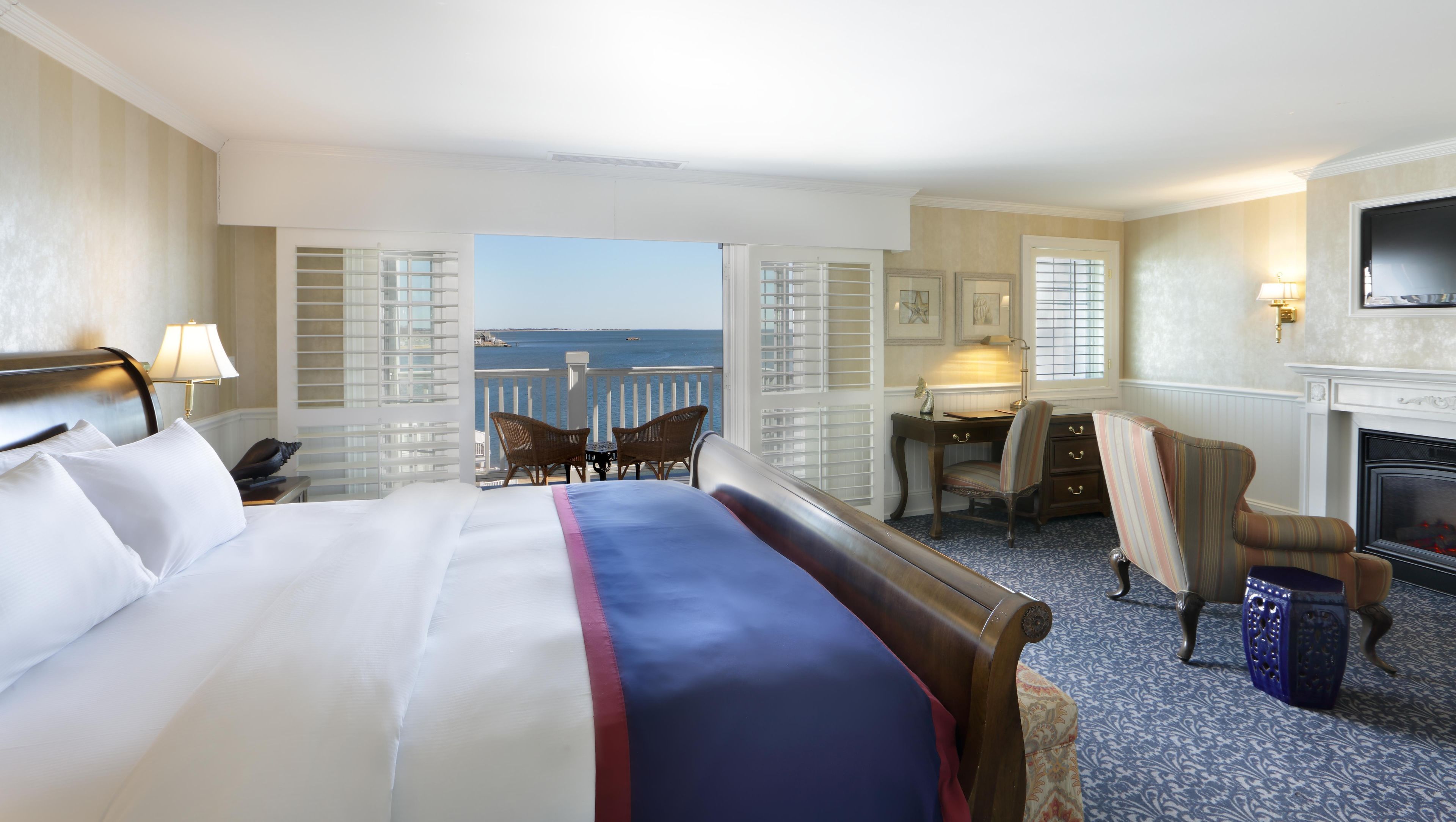 A hotel room with a bed, a desk, a chair, a television, and a view of the sea.