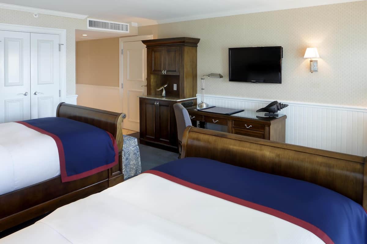 A hotel room with two beds, a desk, a chair, a television, and a wardrobe.