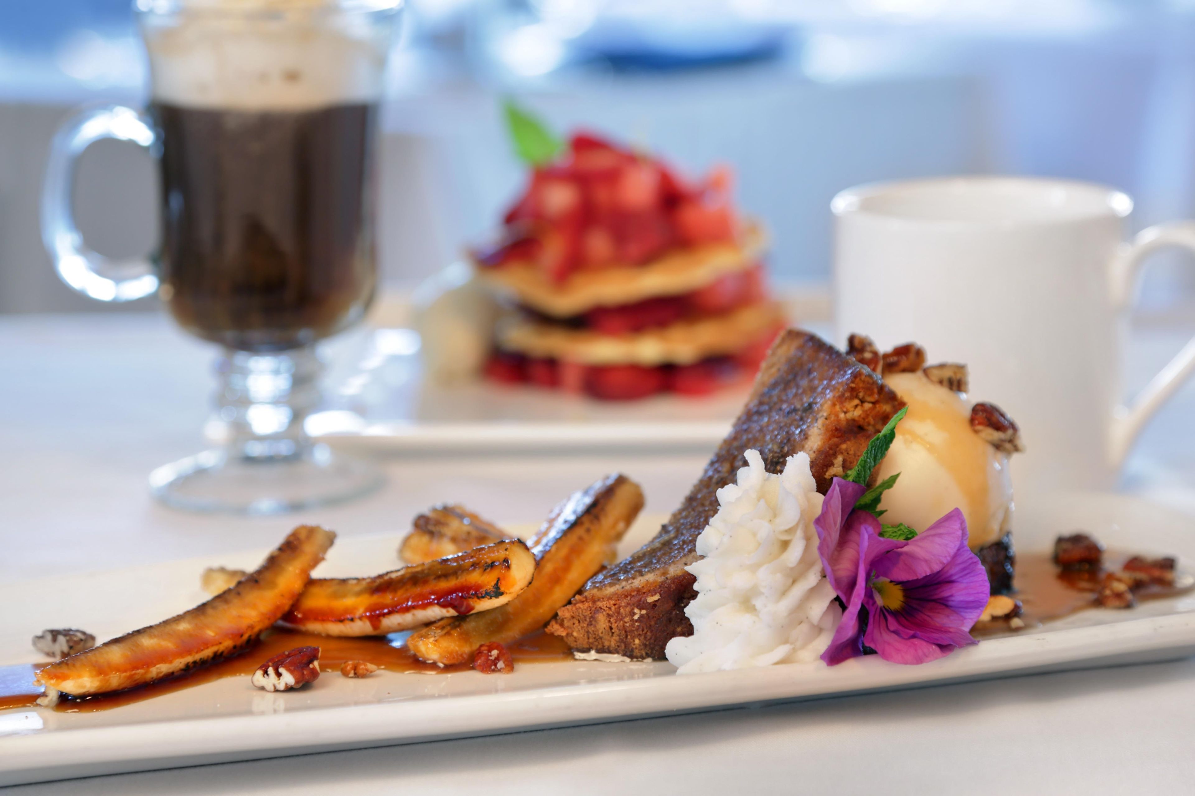 A plate with a dessert, a cup, and a glass of a dark beverage.