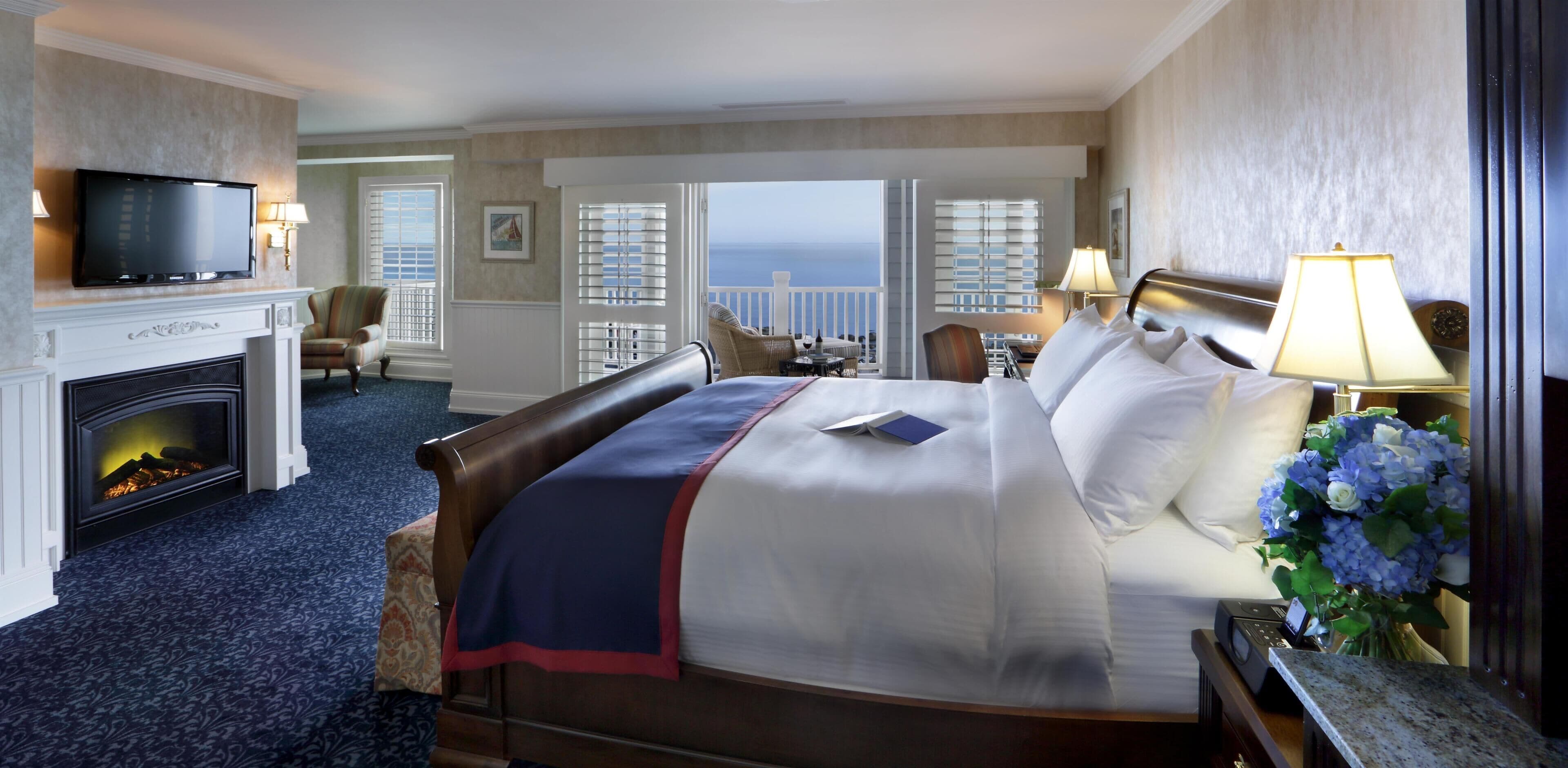 Quarto de hotel com uma cama grande, lareira, televisão e vista para o oceano.