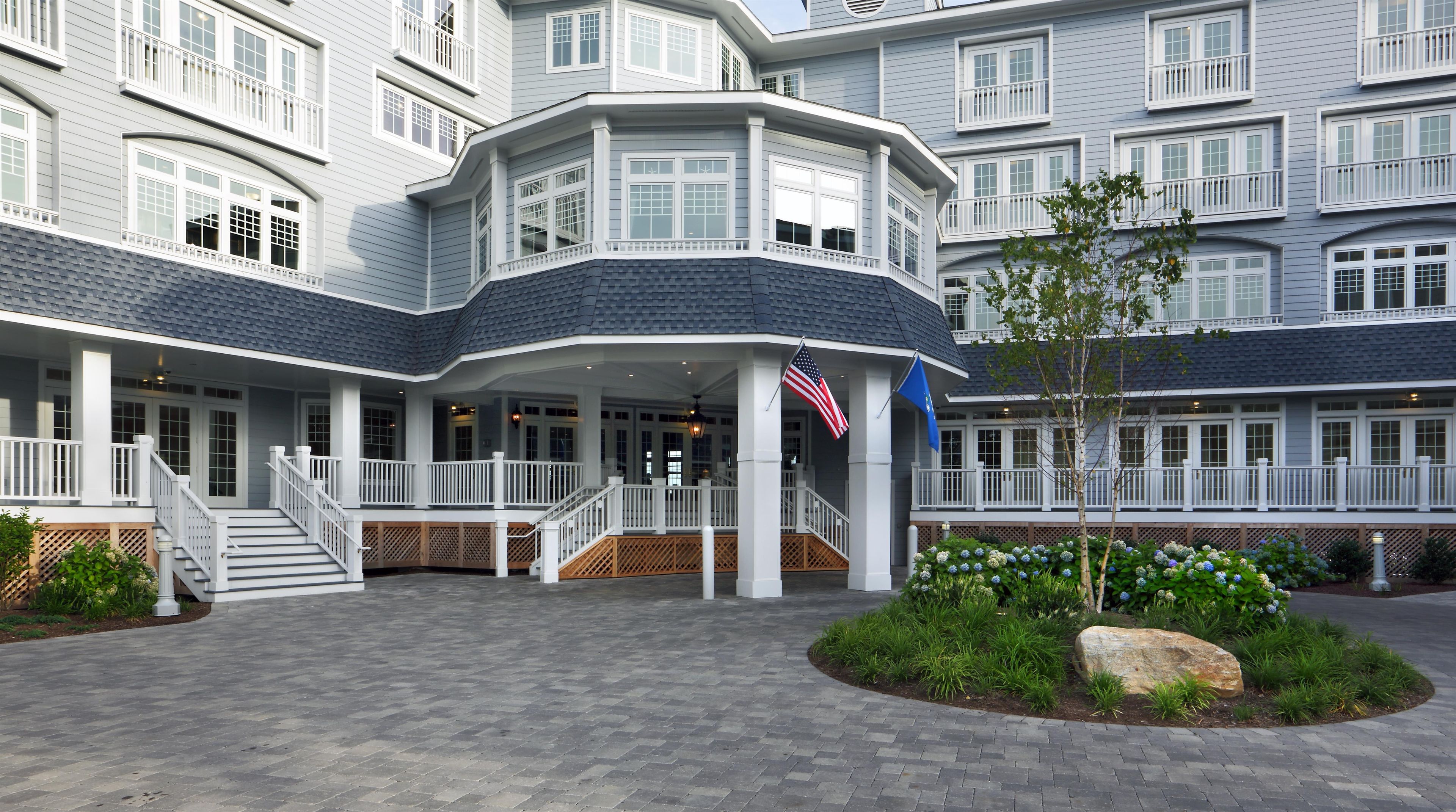Ein mehrstöckiges Hotel mit überdachter Eingangspartie, einer Flagge und einem begrünten Bereich mit Pflanzen und Felsen.