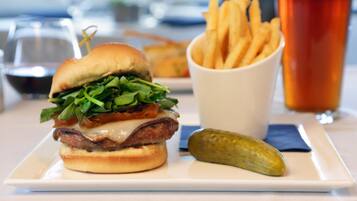 Un hamburger avec des frites et un cornichon, le tout servi sur une assiette blanche, accompagné d’un verre de bière et d’une tasse de café.